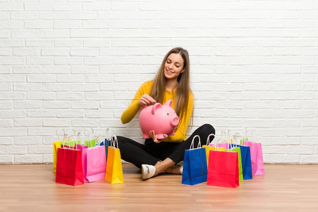 Young girl with lot of shopping bags taking a piggy bank and happy because it is full