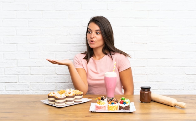 Young girl with lots of different mini cakes holding copyspace imaginary on the palm