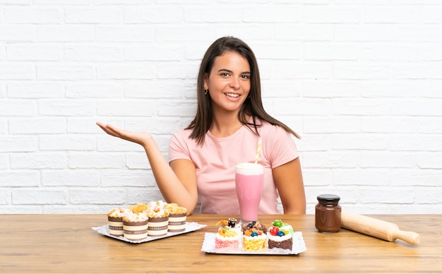 Young girl with lots of different mini cakes holding copyspace imaginary on the palm