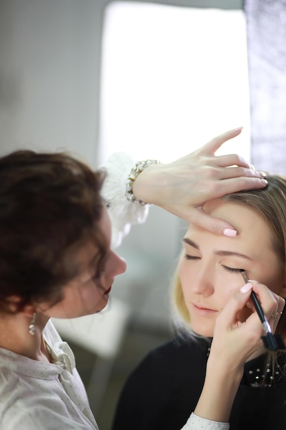 Young girl with a makeup artist in the studio in front of a mirrorxA