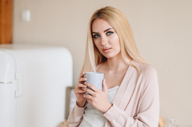 Una giovane ragazza con il trucco sta in cucina con la tazza in mano concetto di essere bella