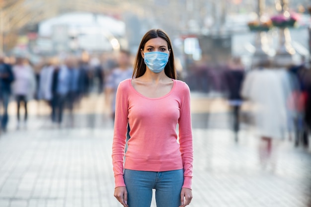 얼굴에 의료 마스크를 쓴 어린 소녀가 붐비는 거리에 서 있다