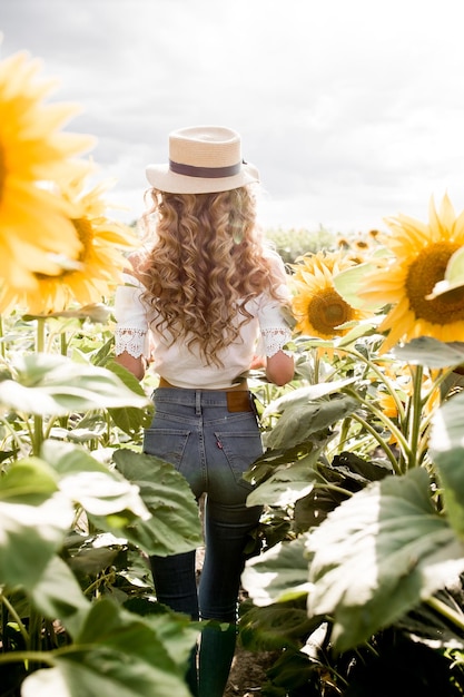 A young girl with a model appearance in denim trousers and a white blouse in a sunflower field