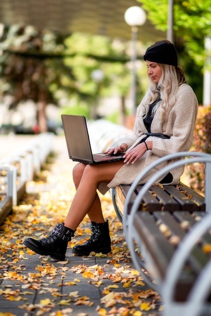 Молодая девушка с блокнотом на ногах сидит в осеннем парке