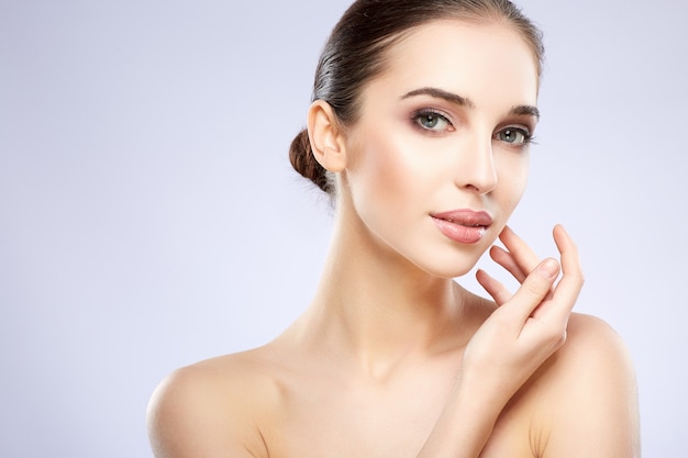 Young  girl with nude make up posing at grey studio background, beauty photo concept, looking at camera, perfect skin.