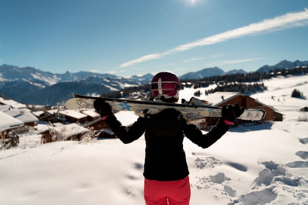 Young girl with a pair of skis and a ski helmet looking at the horizon in a ski resort in the Alps