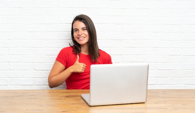 Young girl with pc in a table giving a thumbs up gesture