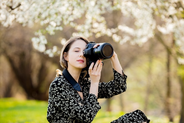 Young girl with photo camera sitting near a flowering tree in the park. Spring season