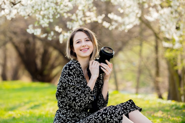 Young girl with photo camera sitting near a flowering tree in the park. Spring season