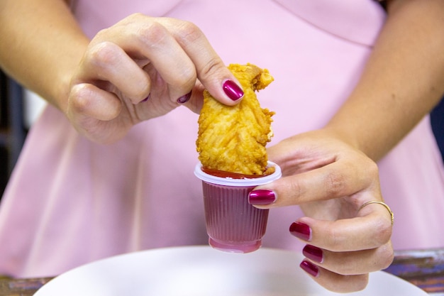 Young girl with piece of chicken in hand dipping it in tomato sauce enclosed view