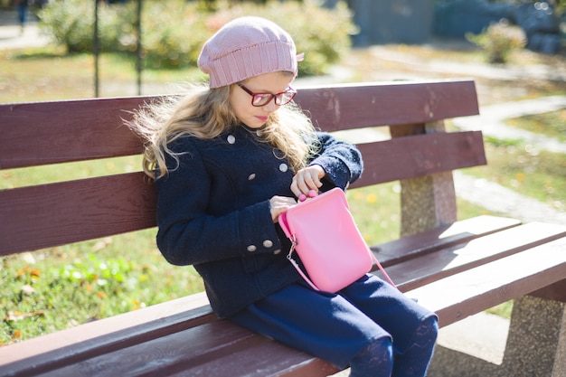 公園のベンチにピンクのハンドバッグを持つ少女