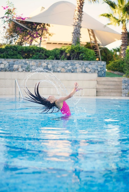 ピンクの水着を着た若い女の子がプールから出てきて、髪をはねかける