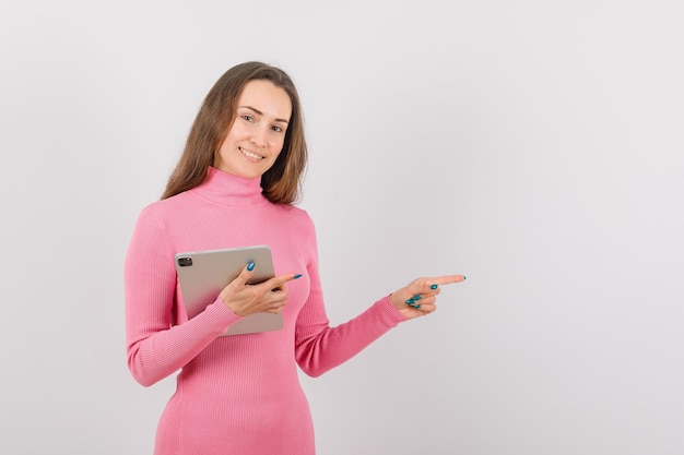 Young girl with planshet computer is pointing to right with other hand on white background