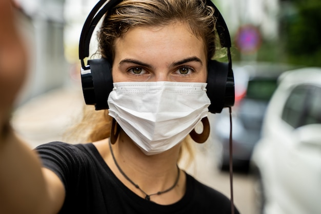 Young girl with a protective mask and headphones to listen to music in the street