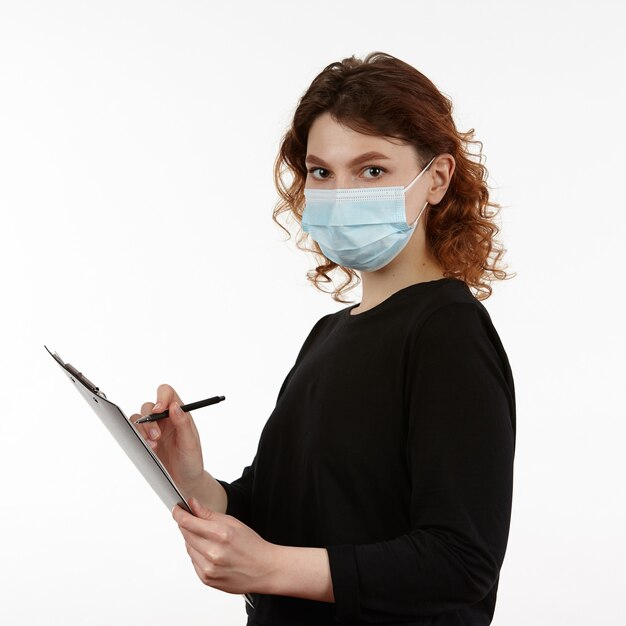 Young girl with a protective mask on her face with a notebook and a pen in her hands.