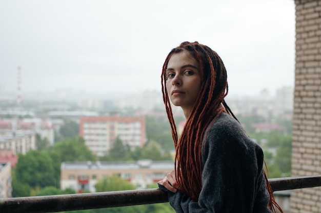 Young girl with red dreadlocks in a gray sweater looking with autumn melancholy mood.