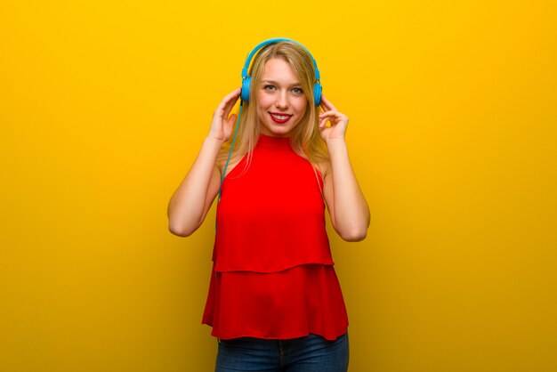 Молодая девушка в красном платье на желтой стене слушает музыку в наушниках