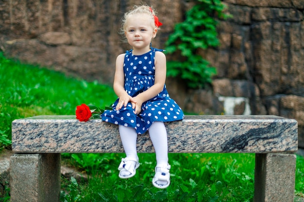 그녀의 손에 장미를 든 어린 소녀가 공원에 앉아 있다