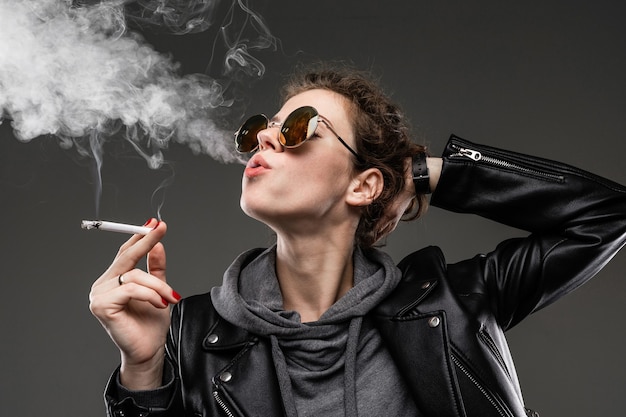 Young girl with rough facial features in black jacket smokes isolated