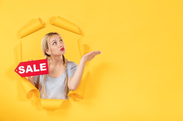 Young girl with sale inscription sign on a torn yellow surface