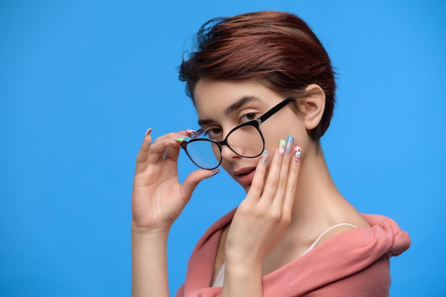 Young girl with short haircut and extravagant nail art looks over the glasses