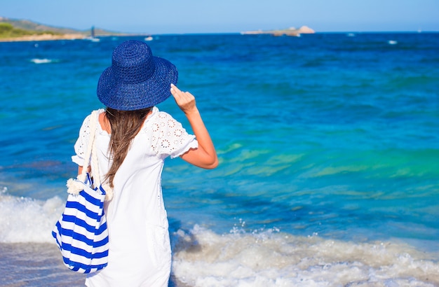 熱帯のビーチで麦わら帽子と青いストライプバッグを持つ若い女の子