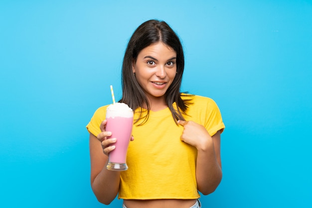 Ragazza con il frappé della fragola sopra la parete isolata con espressione facciale di sorpresa