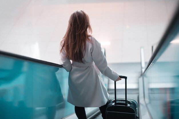 Young girl with suitcase down the escalator.