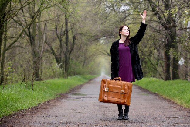 Young girl with suitcase at spring time alley at countryside