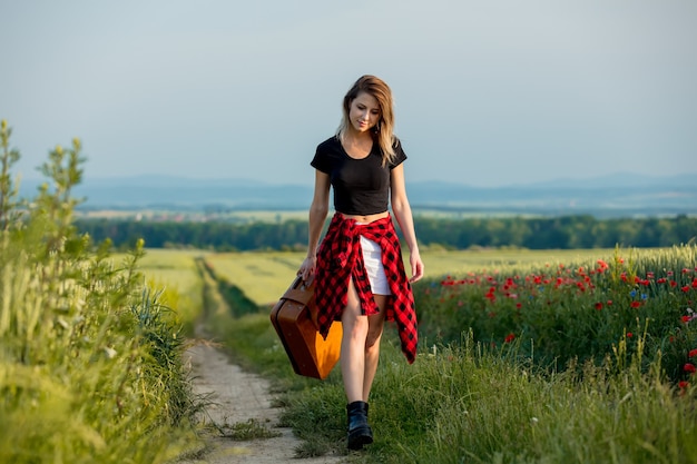 Молодая девушка с чемоданом идет по дороге в сельской местности