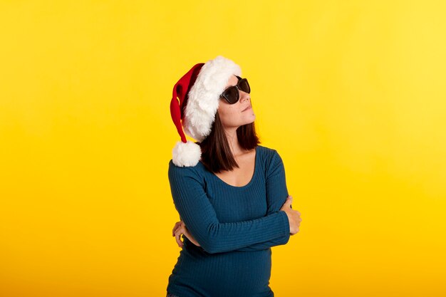 A young girl with sunglasses looking at the camera wearing a santa claus hat