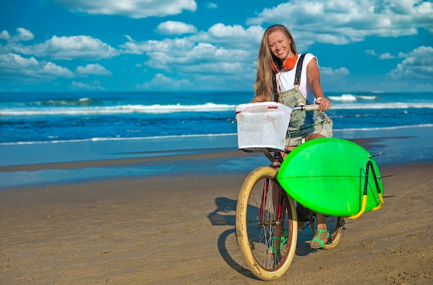 Foto ragazza giovane con tavola da surf e bicicletta sulla spiaggia