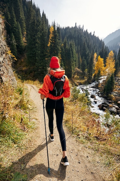 young girl with trekking poles walking at autumn mountain trail