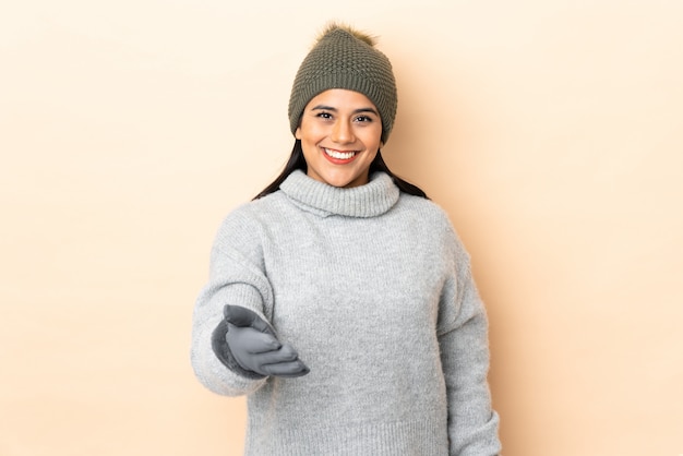 Young girl with winter hat on beige wall handshaking after good deal