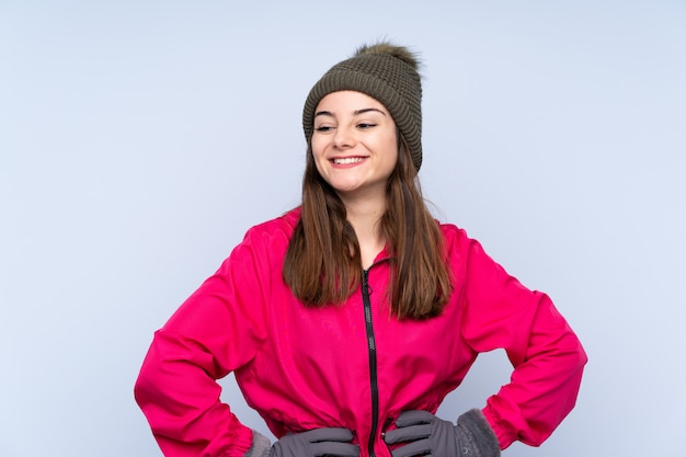 Молодая девушка в зимней шапке на синем позирует с оружием в бедре и улыбается