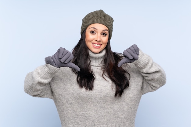 Young girl with winter hat over blue proud and self-satisfied