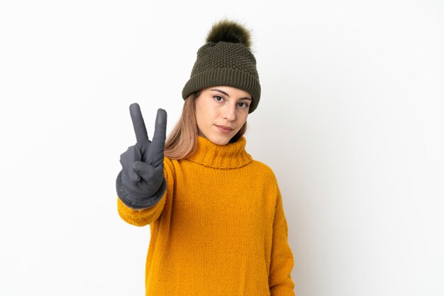Young girl with winter hat isolated on white smiling and showing victory sign