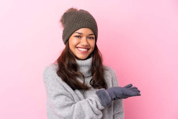 Young girl with winter hat over pink wall extending hands to the side for inviting to come