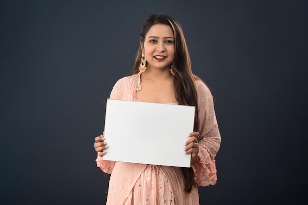 A young girl or woman wearing an Indian traditional dress holding a signboard in her hands on gray background