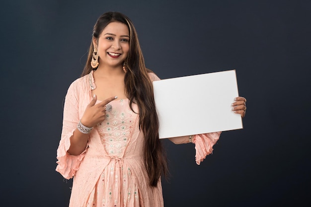 A young girl or woman wearing an Indian traditional dress holding a signboard in her hands on gray background