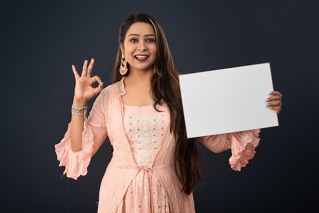 A young girl or woman wearing an Indian traditional dress holding a signboard in her hands on gray background