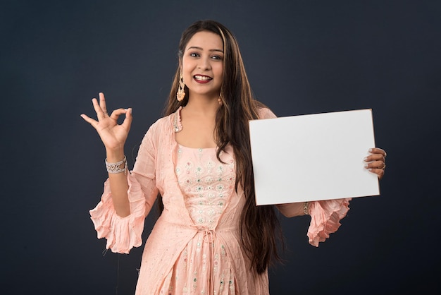 A young girl or woman wearing an Indian traditional dress holding a signboard in her hands on gray background