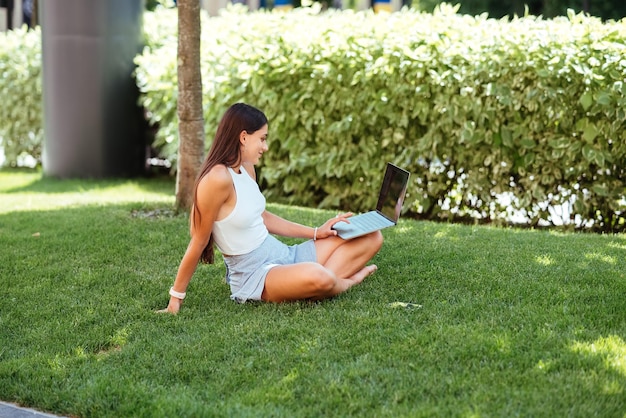 Young girl works with a laptop sitting on the lawn