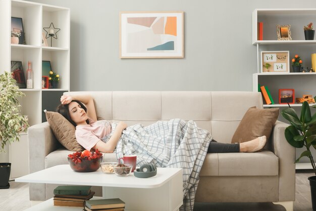 Young girl wrapped in plaid sleeping on sofa behind coffee table in living room