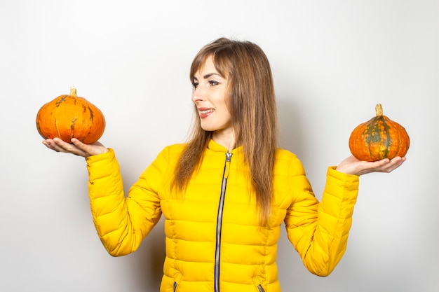 Young girl in a yellow jacket holding two gourd and looking at a pumpkin