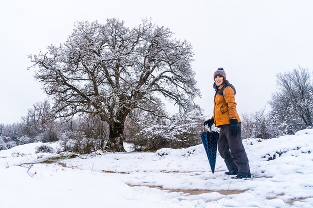 Young girl in a yellow jacket walking through the snow next to a tree. Snow in the town of Opakua near Vitoria in Araba