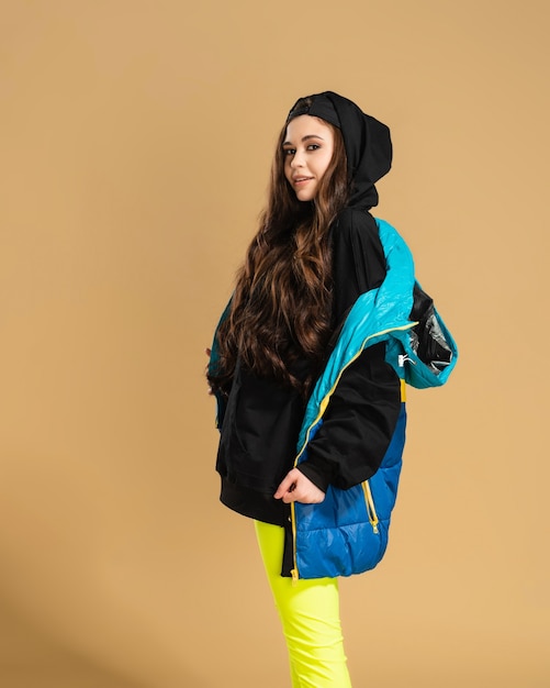 Photo young girl in yellow leggings and a black hoodie and a warm vest posing on a pastel orange.