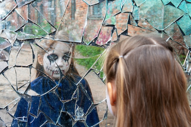 Photo young girl zombie looks in a broken mirror. the concept of human emotions.