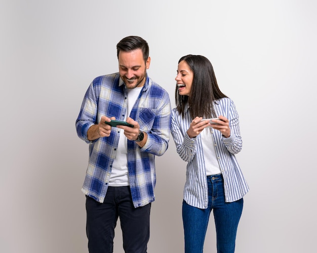 Young girlfriend playing video game and looking cheerfully at boyfriends mobile phone