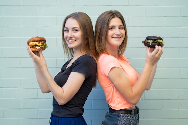 Young girls-students stand eating burgers